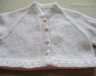 Könnte beinhalten: Weißer gestrickter Baby-Cardigan mit Knopfleiste und rosa Knöpfen.