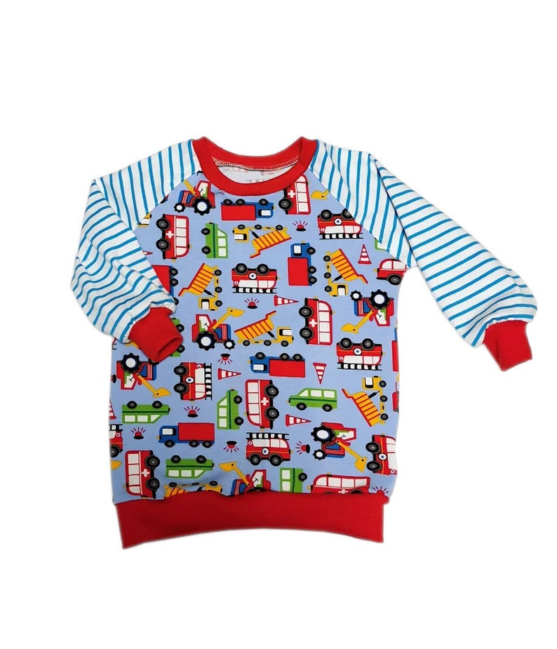 May include: A light blue long-sleeved sweatshirt with a pattern of various vehicles, including trucks and construction equipment. The sleeves are striped blue and white, with red cuffs. The neckline and hem are also red.