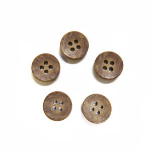 May include: Five round, brown buttons with four holes each, arranged on a white background. The buttons have a textured appearance and a slightly mottled color variation, suggesting a natural material.