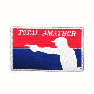 Könnte beinhalten: Ein weißer gestickter Aufnäher mit rotem und blauem Hintergrund. Der Aufnäher zeigt die Silhouette einer Person, die eine Waffe hält, und den Text "TOTAL AMATEUR".