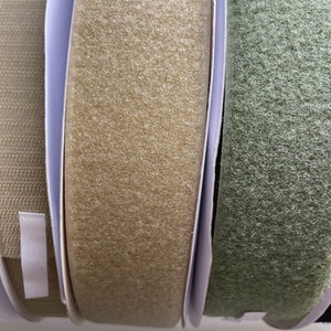 May include: Close-up of three rolls of hook and loop tape. The tape is beige, green, and tan. The tape is rolled up and is ready to be used for crafts, sewing, or other projects.