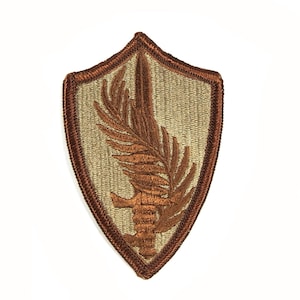 May include: A brown embroidered patch with a tan background. The patch is shaped like a shield and features a stylized brown leaf with a sword through it.