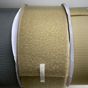 Puede incluir: Primer plano de un rollo de cinta de velcro beige. La cinta está envuelta alrededor de un núcleo de cartón blanco.