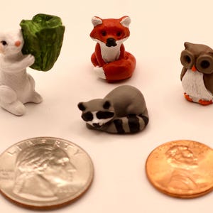 May include: Miniature figurines of woodland animals, including a white dog holding a green cabbage, a red fox, a raccoon, and an owl. A quarter and a penny are included for size reference.