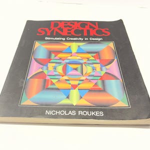 May include: A softcover book titled Design Synectics: Stimulating Creativity in Design by Nicholas Roukes. The black cover features a large, square, multi-colored geometric pattern with vibrant gradients of red, blue, yellow, and green shapes.