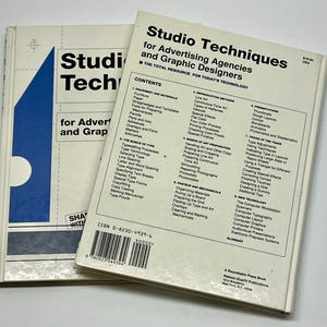May include: Two vintage books titled "Studio Techniques for Advertising Agencies and Graphic Designers" are stacked. The books have white covers with black text and a blue and white graphic. The contents and ISBN are visible.