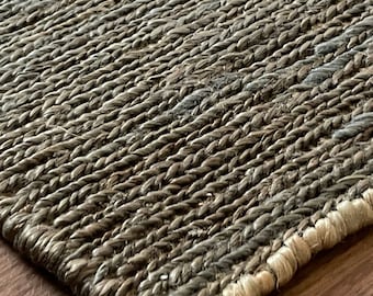 May include: Close-up of a woven rug with a natural, earthy colour palette. The rug has a textured, hand-woven look and a frayed edge.