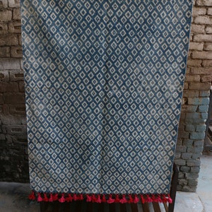 Peut inclure: Un tapis bleu et blanc &agrave; motifs avec des glands roses. Le tapis est accroch&eacute; &agrave; un mur en briques.