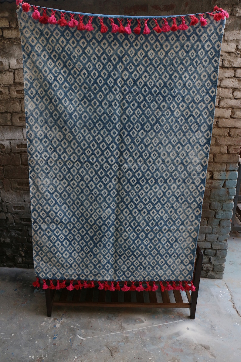 Peut inclure: Un tapis bleu et blanc &agrave; motifs avec des glands roses. Le tapis est accroch&eacute; &agrave; un mur en briques.