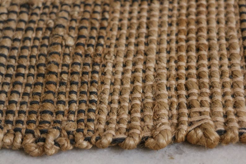 K&ouml;nnte beinhalten: Nahaufnahme eines gewebten Teppichs in nat&uuml;rlichen Braun- und Schwarzt&ouml;nen. Der Teppich besteht aus einem dicken, strukturierten Material und hat eine leicht raue Oberfl&auml;che.