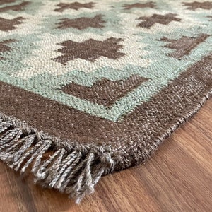 May include: A brown and green woven rug with a geometric pattern and fringe on the edges.