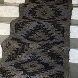 K&ouml;nnte beinhalten: Ein schwarz-grauer Teppich mit geometrischem Muster. Der Teppich ist aus einem gewebten Material gefertigt und hat einen Fransenrand. Der Teppich liegt auf einer Treppe.