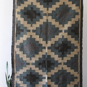 May include: A blue and beige geometric patterned rug with a fringe border. The rug is made of natural fibers and has a rustic look.