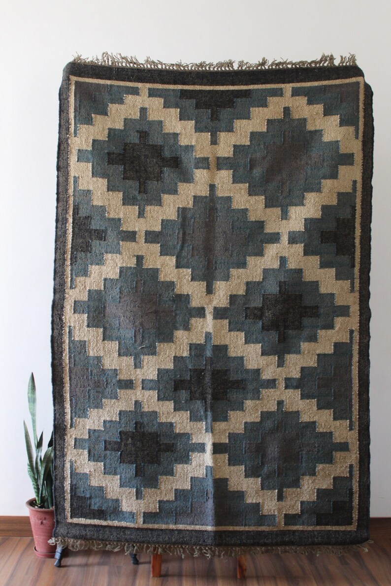 May include: A blue and beige geometric patterned rug with a fringe border. The rug is made of natural fibers and has a rustic look.