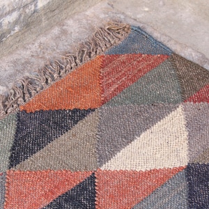 May include: A geometric patterned rug with a fringe border. The rug is made of woven fabric in shades of brown, gray, black, and red.