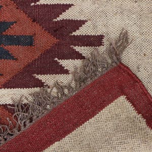 May include: A close-up of a woven rug with a geometric pattern in shades of brown, red, and white. The rug has a fringe border.