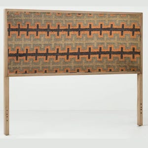 May include: Wooden headboard featuring a geometric pattern in orange, black, and green. The headboard has a rectangular shape with a wooden frame and two legs. The patterned fabric is stretched across the frame. The headboard measures approximately 150cm in width.