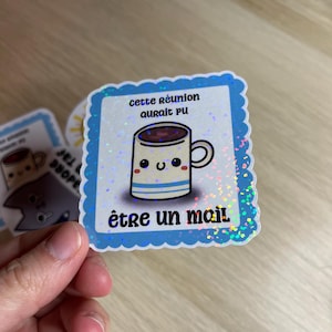 Può includere: Un adesivo blu e bianco con una finitura scintillante. L'adesivo presenta una tazza di cartone animato con un viso sorridente e il testo "cette réunion aurait pu être un mail".