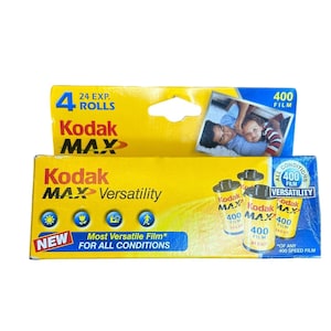 Puede incluir: Un paquete de rollos de película Kodak Max 400. El embalaje es amarillo y azul, con el logotipo de Kodak Max. El paquete indica 4 rollos de película, con una foto de un padre y un niño. El texto dice "Película más versátil para todas las condiciones."
