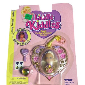 May include: A Liddle Kiddles Lovely Locket Debbie Dance Party doll set in original packaging. The set includes a small blonde doll inside a heart-shaped gold and purple locket, a purple hairbrush, and four small star and heart-shaped stickers.