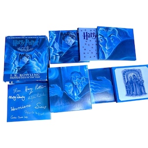 Puede incluir: Una colección de estuches de discos compactos de audiolibros de Harry Potter y la Orden del Fénix en tonos azules. El conjunto incluye una caja, estuches individuales con ilustraciones de personajes y un estuche cuadrado azul con nombres.