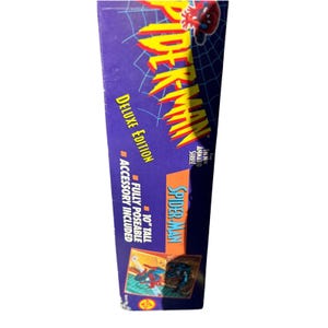 Puede incluir: Una caja de figura de acci&oacute;n de Spider-Man morada y naranja. La caja presenta el logotipo de Spider-Man en amarillo y rojo, con las palabras "Deluxe Edition" y "Accessory Included". La figura mide 25,4 cm de alto y es totalmente articulada.