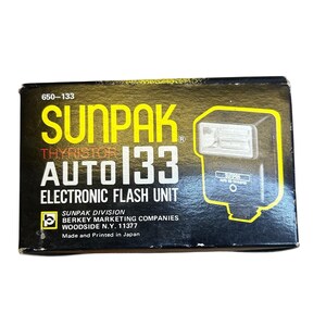 May include: A black and gold box for a Sunpak Auto 133 electronic flash unit. The box features the brand name "SUNPAK" in large yellow letters, along with the model number and a graphic of the flash unit. The text "Made and Printed in Japan" is also visible.