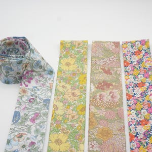 May include: A collection of floral patterned fabric strips in various colors. One strip is rolled up, displaying a blue, purple, and white floral design. Other strips feature yellow, pink, and orange floral patterns. The fabrics are likely for crafting or sewing projects.