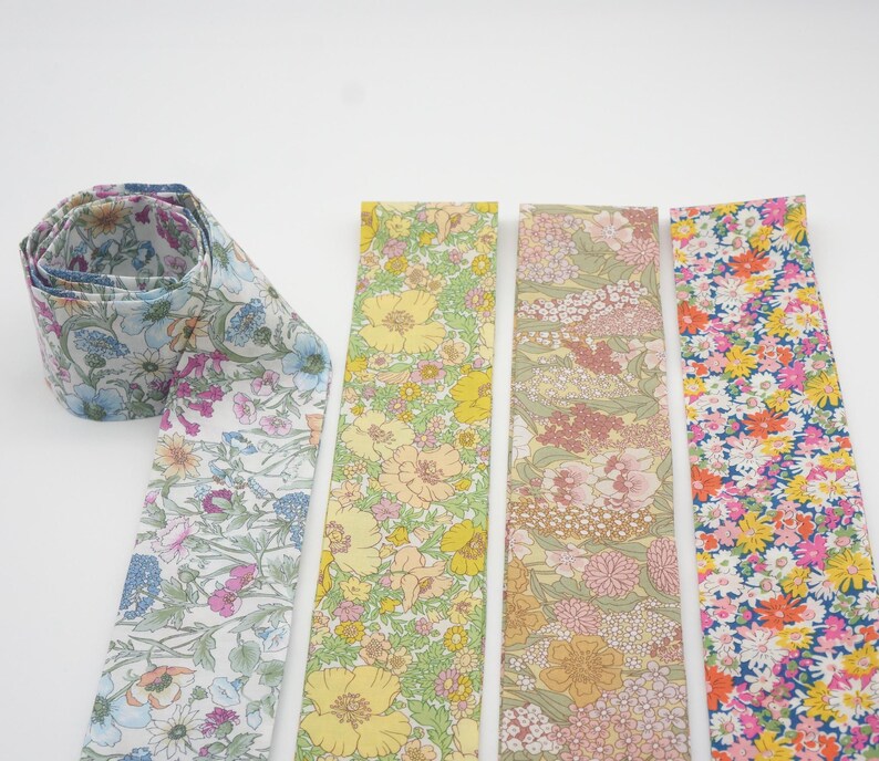 May include: A collection of floral patterned fabric strips in various colors. One strip is rolled up, displaying a blue, purple, and white floral design. Other strips feature yellow, pink, and orange floral patterns. The fabrics are likely for crafting or sewing projects.