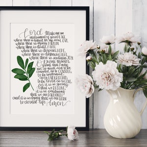 May include: A printable wall art design featuring a handwritten quote about being an instrument of peace, love, pardon, faith, hope, light, joy, and understanding. The quote is written in black ink on a white background with a green watercolour leaf illustration.