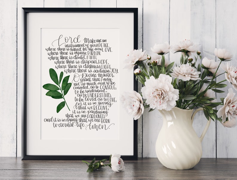 May include: A printable wall art design featuring a handwritten quote about being an instrument of peace, love, pardon, faith, hope, light, joy, and understanding. The quote is written in black ink on a white background with a green watercolour leaf illustration.