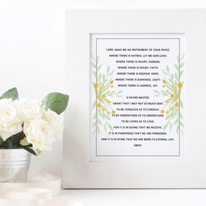 May include: A framed print with a white background and green and yellow floral accents. The print features a prayer for peace, asking to be an instrument of peace, love, pardon, faith, hope, light, and joy. The prayer ends with "O Divine Master, grant that I may not so much seek to be consoled as to console, to be understood as to understand, to be loved as to love. For it is in giving that we receive, it is in pardoning that we are pardoned, and it is in dying that we are born to eternal life. Amen."
