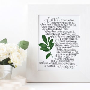 May include: A white framed print with a green leaf design and a black and white text quote. The quote reads "Lord make me an instrument of your peace...and it is in dying that we are born to eternal life. Amen."