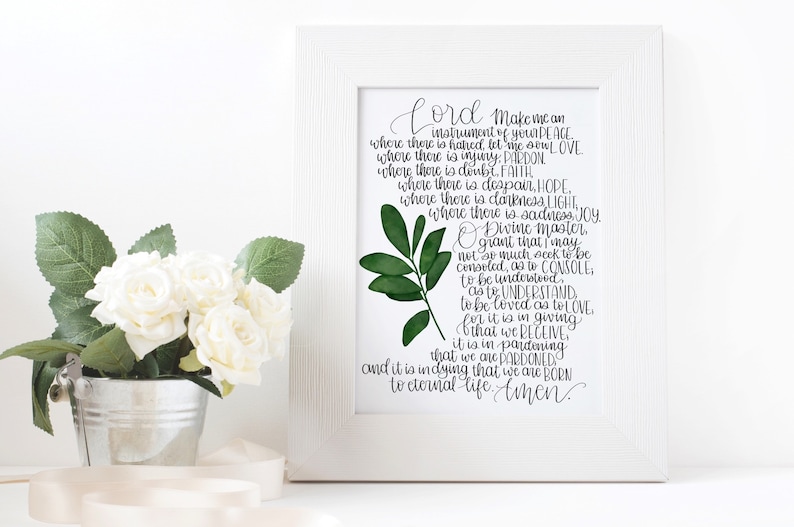 May include: A white framed print with a green leaf design and a black and white text quote. The quote reads "Lord make me an instrument of your peace...and it is in dying that we are born to eternal life. Amen."