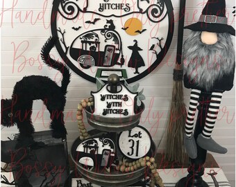 May include: A three-tiered metal stand with a black and white Halloween theme. The top tier has a round sign that says "Lot 31" and wooden beads. The middle tier has a sign that says "Witches with Hitches" and a black cat silhouette. The bottom tier has a sign that says "Best Hitches Witches" and a sign with crossed broomsticks.