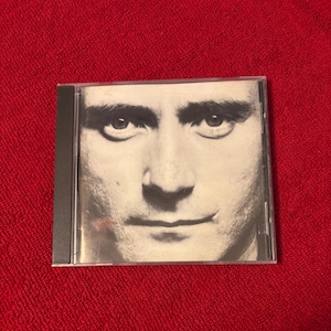 May include: A CD case featuring a black and white close-up of a person's face. The image is centered on the face, with the eyes and mouth clearly visible. The case is rectangular and made of clear plastic.