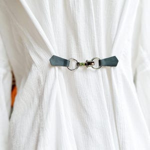 May include: A white shirt with a black leather strap and silver metal buckle closure.