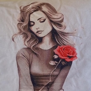 Puede incluir: Un diseño de punto de cruz que presenta a una mujer con cabello castaño suelto y una rosa roja. La mujer lleva una blusa marrón. La imagen está sobre un fondo blanco.