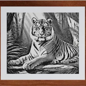 Puede incluir: Un patrón de punto de cruz en blanco y negro enmarcado que muestra a un tigre descansando en un entorno de selva densa con helechos y árboles. La obra está realizada en estilo punteado, dentro de un marco de madera marrón con un borde blanco.