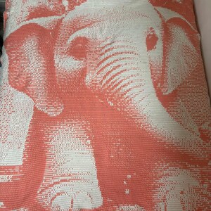 May include: A coral and white crochet blanket featuring a detailed elephant design. The blanket showcases a pixelated image of an elephant's head and trunk. The color palette is a combination of coral and white, creating a striking contrast.