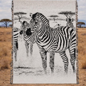 Może przedstawiać: Tkany koc z czarno-białym wzorem zebry. Koc przedstawia zebry w krajobrazie sawanny z drzewami i zachmurzonym niebem. Prostokątny koc ma frędzle na krawędziach.