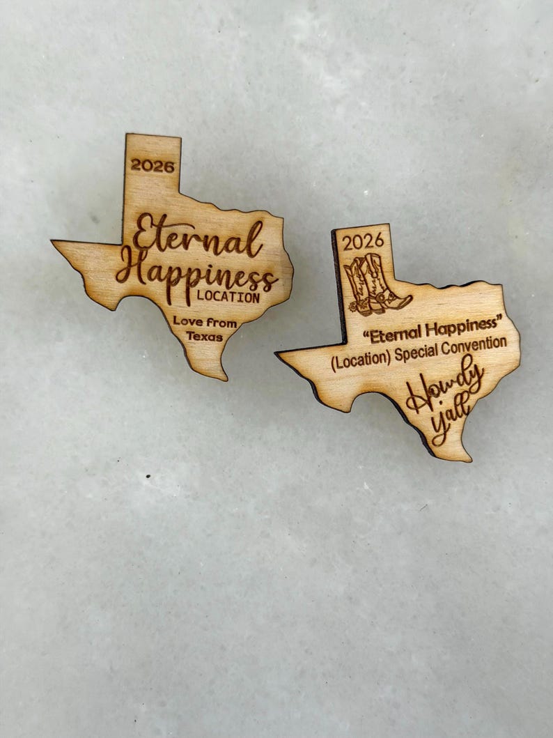 May include: Two wooden Texas-shaped ornaments. One reads "Eternal Happiness" with "Love From Texas" and the year "2026". The other says "Eternal Happiness" with "Howdy Y'all" and the year "2026".