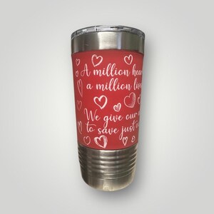 May include: A red stainless steel tumbler with a white inscription that reads "A million hearts, a million lives. We give our all to save just one." The tumbler is decorated with white hearts.