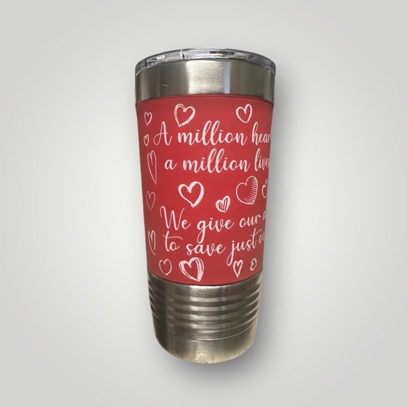 May include: A red stainless steel tumbler with a white inscription that reads "A million hearts, a million lives. We give our all to save just one." The tumbler is decorated with white hearts.