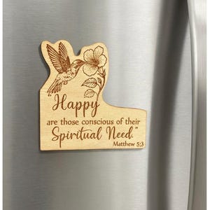 May include: Wooden fridge magnet with a hummingbird and flower design. The magnet is engraved with the words "Happy are those conscious of their Spiritual Need." and the Bible verse Matthew 5:3.