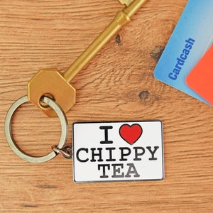 May include: A gold key with a silver key ring attached to a white metal keychain with the text "I ♥ CHIPPY TEA".