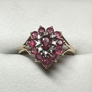 May include: A gold ring featuring a cluster of pink gemstones and smaller white gemstones arranged in a flower-like design.