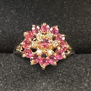 May include: A gold ring with a cluster of pink gemstones set in a flower shape.
