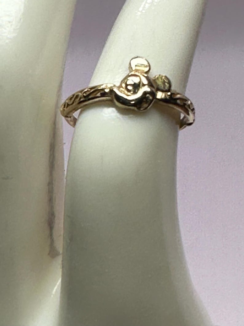 May include: Gold ring with a detailed design featuring a small Mickey Mouse head.