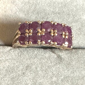 May include: A silver ring with a band of purple gemstones. The ring is set with multiple small, square-shaped stones.